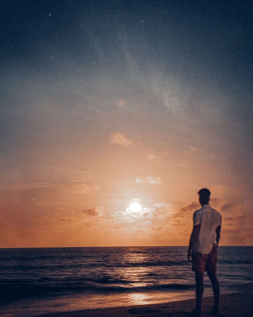 A person quietly watching the night sky over the ocean, reflecting on the mystery of consciousness.