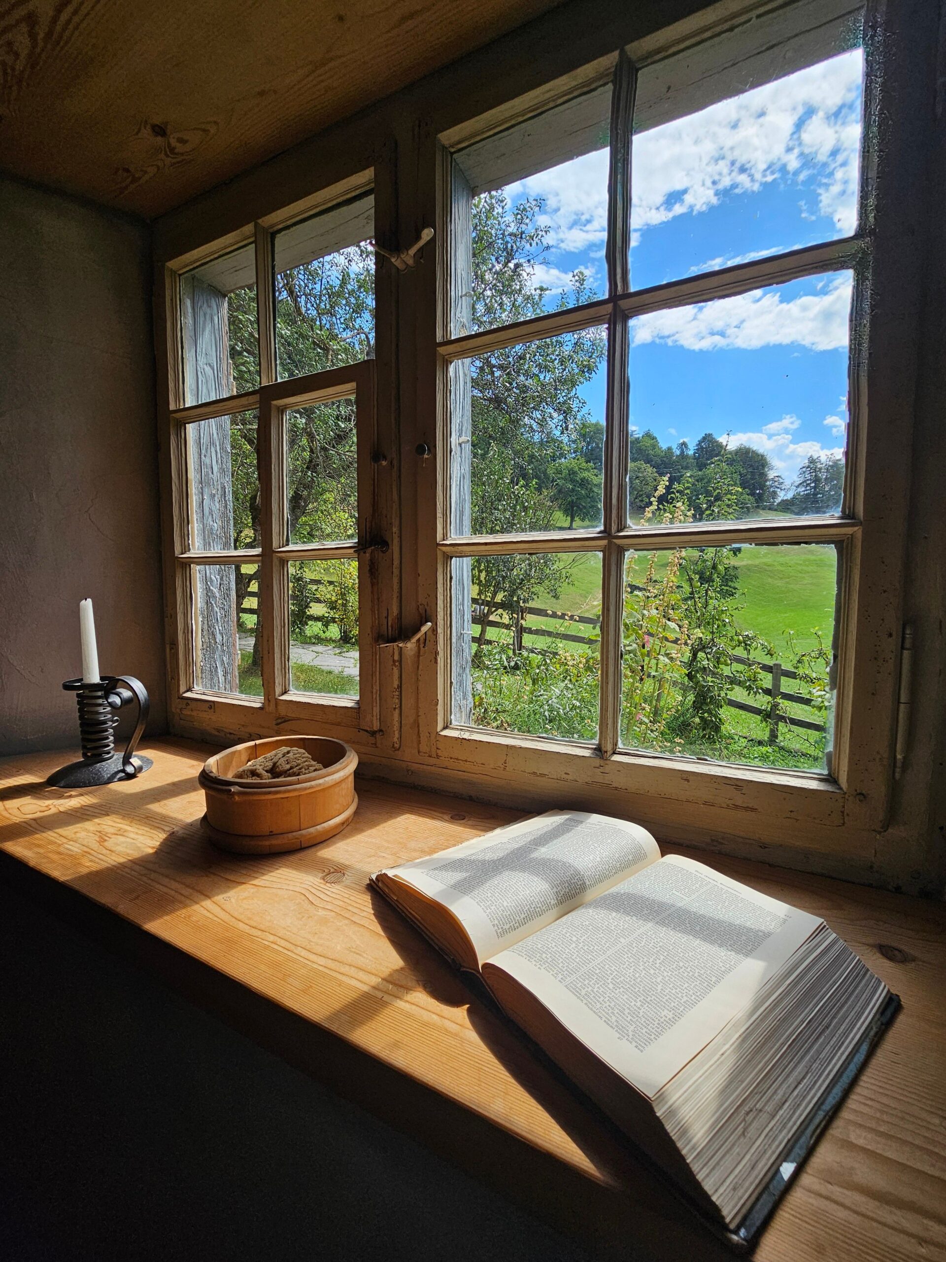 An open book beside a sunlit window overlooking a peaceful countryside, reflecting calm focus, quiet reflection, and mindful learning.